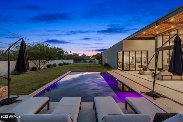 pool at dusk featuring a lawn and a patio area