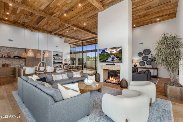 living room with wooden ceiling, light wood-type flooring, a towering ceiling, a fireplace, and beamed ceiling