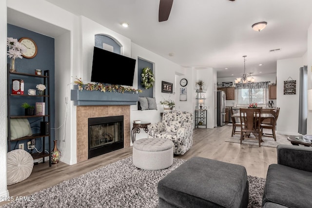 living room featuring ceiling fan with notable chandelier, a tile fireplace, and light wood-type flooring