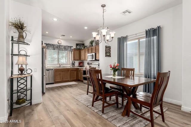 dining space with sink, an inviting chandelier, and light wood-type flooring