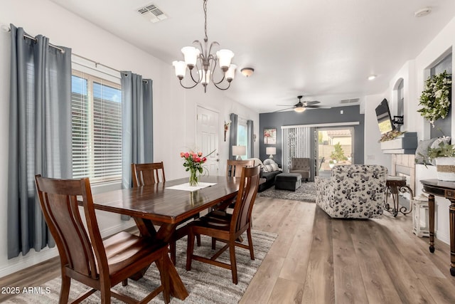 dining space with ceiling fan with notable chandelier and light hardwood / wood-style floors