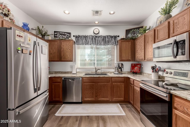 kitchen with sink, light hardwood / wood-style flooring, light stone countertops, and appliances with stainless steel finishes