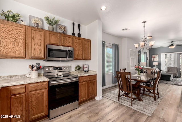 kitchen featuring pendant lighting, appliances with stainless steel finishes, light stone countertops, and light hardwood / wood-style floors