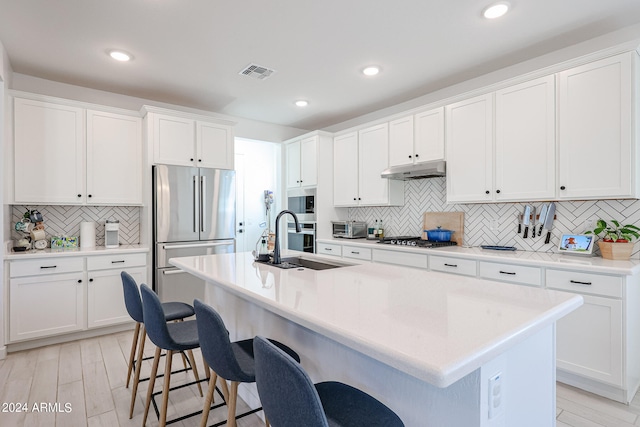 kitchen featuring light hardwood / wood-style floors, a breakfast bar area, an island with sink, white cabinets, and stainless steel appliances