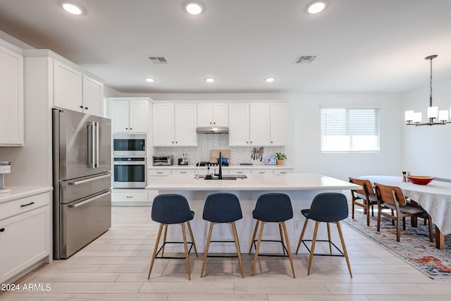 kitchen featuring an island with sink, white cabinets, pendant lighting, high quality fridge, and sink