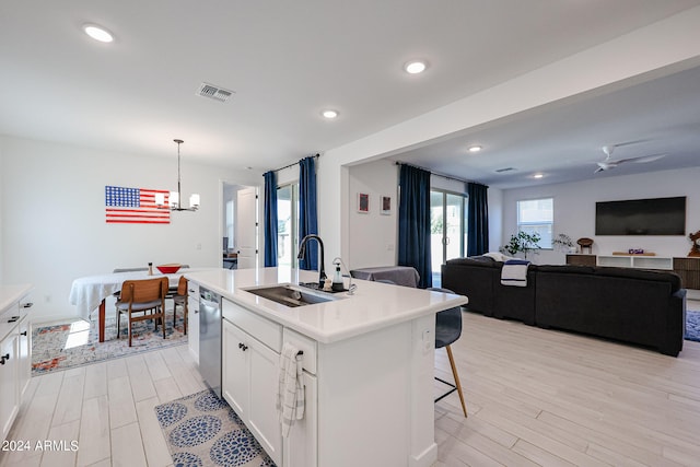 kitchen featuring pendant lighting, an island with sink, white cabinets, stainless steel dishwasher, and ceiling fan with notable chandelier