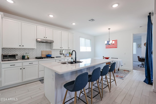 kitchen featuring hanging light fixtures, a breakfast bar, white cabinets, a center island with sink, and sink