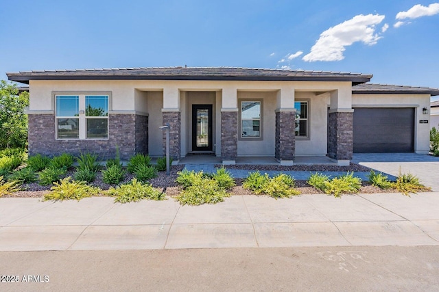 prairie-style home featuring stone siding, stucco siding, an attached garage, and driveway