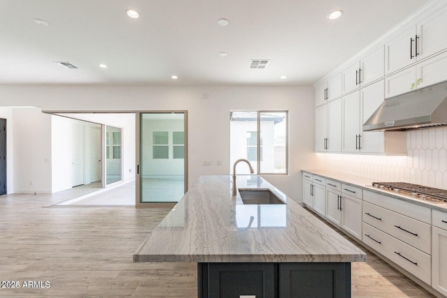 kitchen featuring visible vents, under cabinet range hood, a center island with sink, stainless steel gas stovetop, and a sink