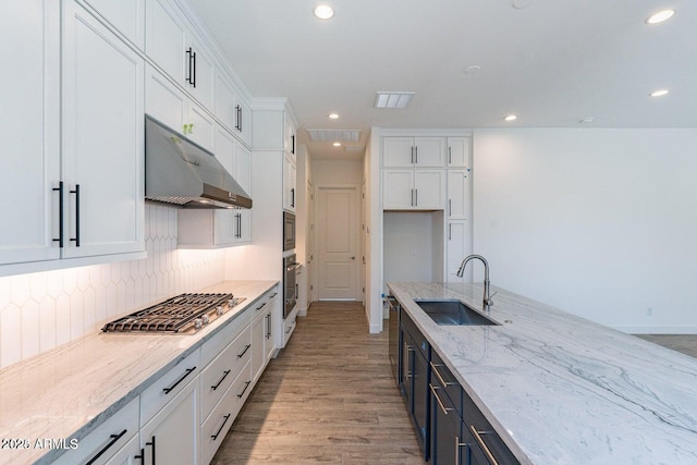 kitchen featuring stainless steel appliances, a sink, white cabinets, under cabinet range hood, and tasteful backsplash