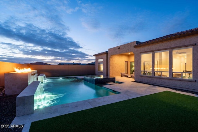 pool at dusk featuring a patio, pool water feature, and an in ground hot tub