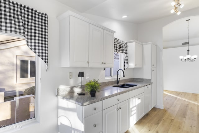 kitchen with white cabinetry, sink, decorative light fixtures, and light wood-type flooring