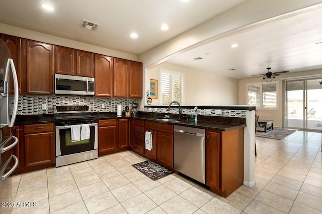 kitchen featuring sink, dark stone countertops, light tile patterned floors, kitchen peninsula, and stainless steel appliances