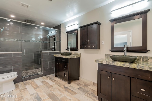 full bath featuring a sink, toilet, two vanities, and a shower stall