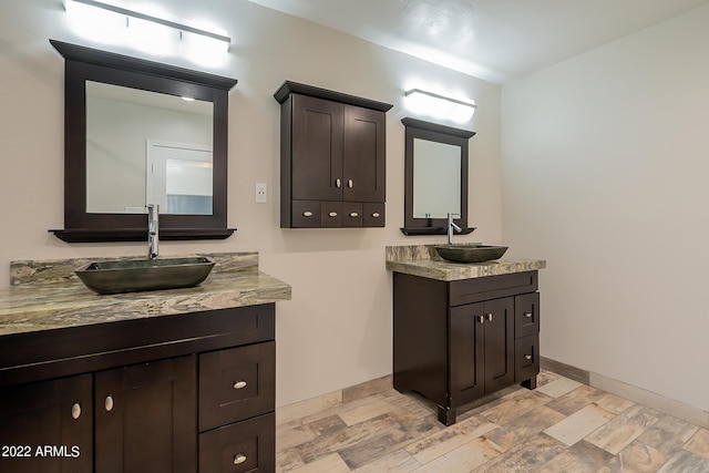 full bathroom featuring wood finished floors, two vanities, baseboards, and a sink