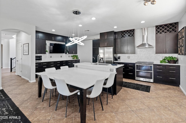 4418 W Yoosooni Dr, New River, AZ 85087 - kitchen featuring appliances with stainless steel finishes, wall chimney exhaust hood, decorative backsplash, light countertops, and arched walkways