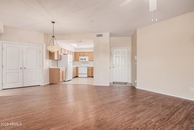 unfurnished living room featuring ceiling fan, a tray ceiling, and light wood-type flooring