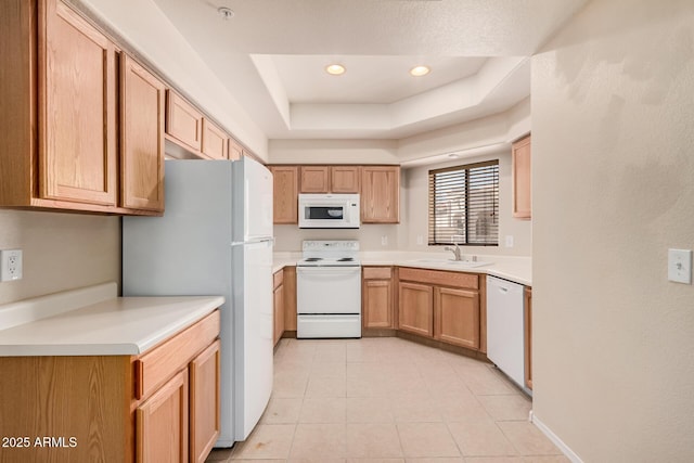 kitchen with a tray ceiling, sink, white appliances, and light tile patterned floors