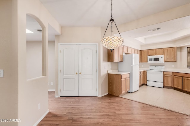 kitchen featuring pendant lighting, white appliances, a raised ceiling, and light wood-type flooring