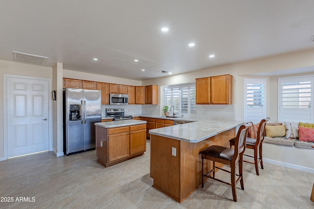 kitchen featuring kitchen peninsula, stainless steel appliances, a kitchen island, a breakfast bar area, and sink