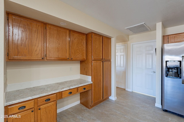 kitchen featuring built in desk, light stone counters, and stainless steel refrigerator with ice dispenser