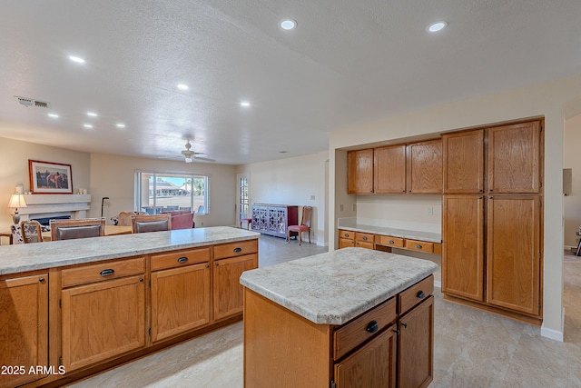 kitchen with light stone countertops, a textured ceiling, ceiling fan, and a center island