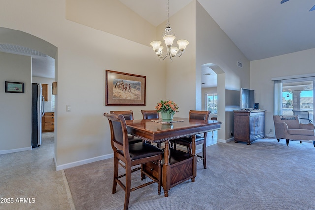 dining room with high vaulted ceiling, plenty of natural light, light carpet, and a chandelier