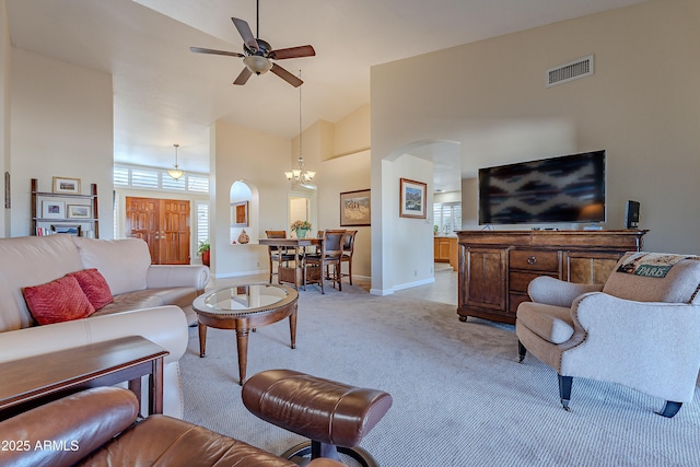 carpeted living room featuring ceiling fan with notable chandelier and high vaulted ceiling