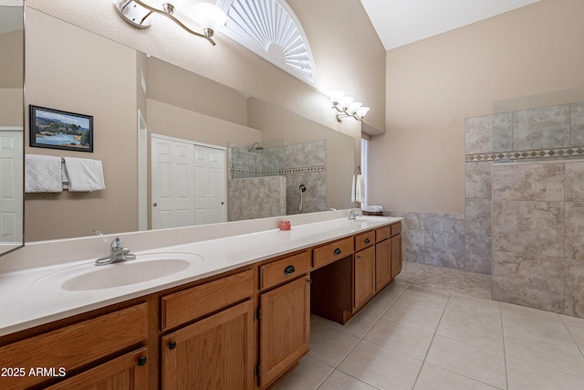 bathroom with lofted ceiling, tile patterned floors, a tile shower, and vanity