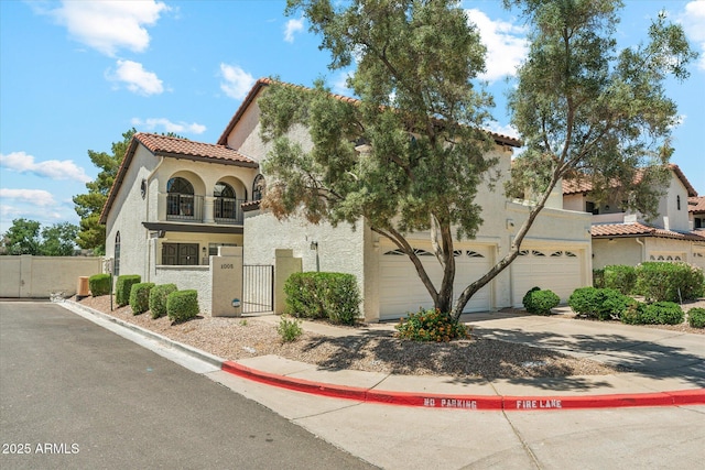 mediterranean / spanish home featuring stucco siding, a garage, driveway, fence, and a gate