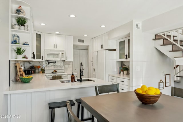 kitchen featuring white appliances, open shelves, a peninsula, a sink, and white cabinetry