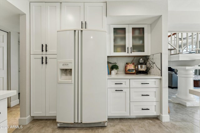 kitchen featuring white fridge with ice dispenser, white cabinetry, light countertops, and glass insert cabinets