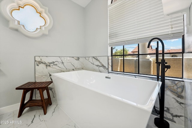 full bathroom featuring marble finish floors, tile walls, a freestanding tub, and a wainscoted wall