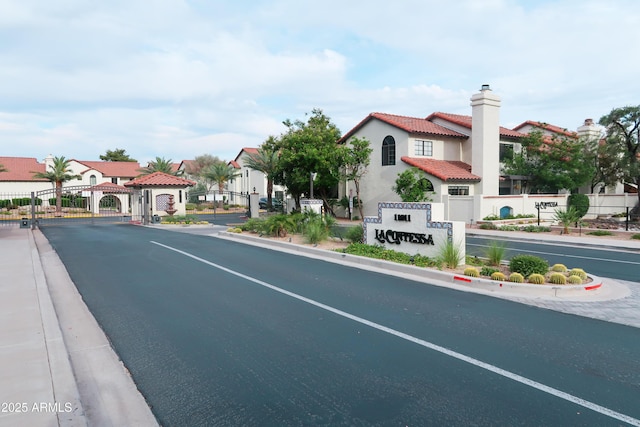 view of asphalt road with curbs, a gate, a gated entry, and street lighting