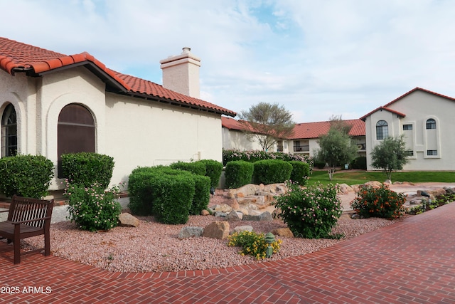 view of property exterior featuring a chimney, stucco siding, and a tiled roof