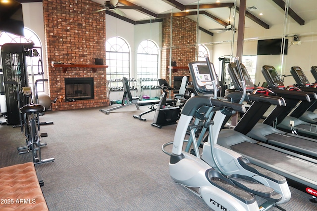 workout area with ceiling fan, beam ceiling, a brick fireplace, high vaulted ceiling, and carpet flooring