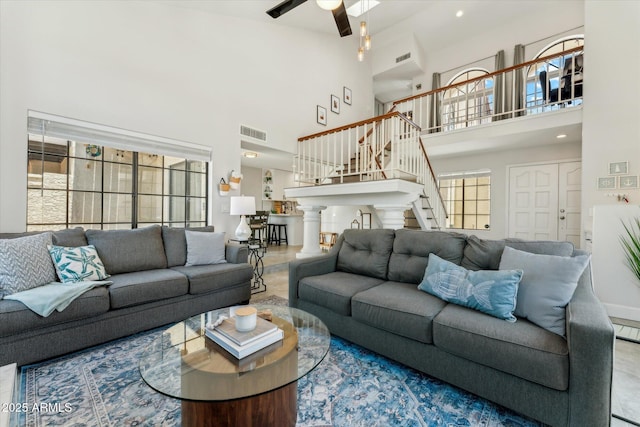 living area with a towering ceiling, ceiling fan, and stairs