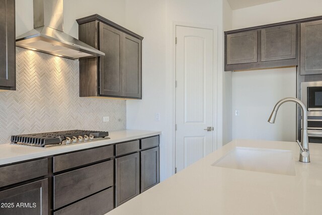 kitchen with tasteful backsplash, sink, dark brown cabinetry, stainless steel appliances, and wall chimney exhaust hood