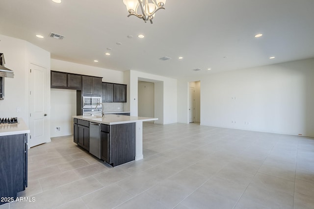 kitchen with an island with sink, sink, dark brown cabinetry, stainless steel appliances, and an inviting chandelier