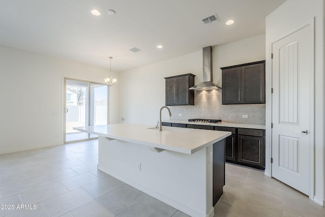 kitchen with wall chimney exhaust hood, sink, hanging light fixtures, a center island with sink, and backsplash