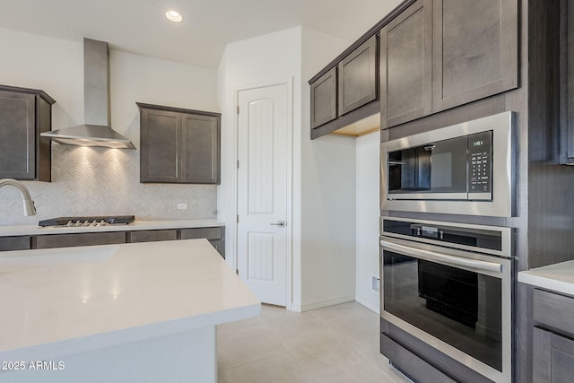 kitchen with built in microwave, decorative backsplash, stainless steel oven, dark brown cabinetry, and wall chimney range hood