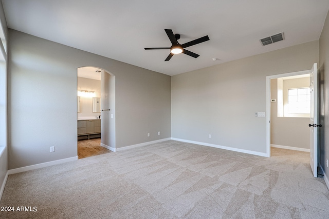 unfurnished bedroom with ensuite bathroom, light carpet, and ceiling fan