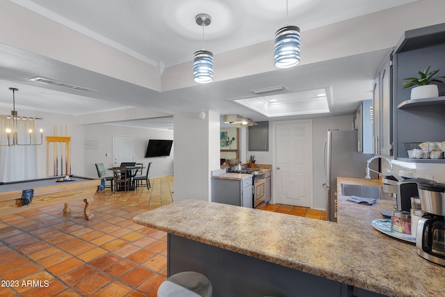 kitchen featuring stainless steel gas range oven, billiards, a tray ceiling, decorative light fixtures, and kitchen peninsula