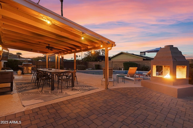 patio terrace at dusk with a fenced in pool and an outdoor fireplace