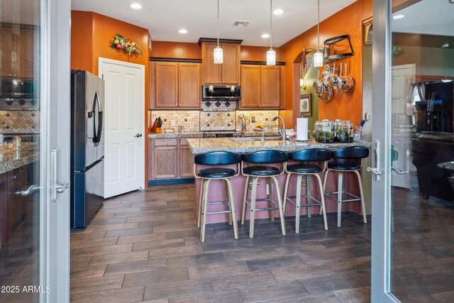 kitchen featuring light stone counters, appliances with stainless steel finishes, a peninsula, brown cabinetry, and decorative backsplash