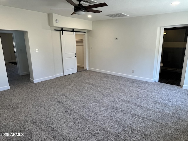 unfurnished bedroom with ceiling fan, a barn door, ensuite bathroom, carpet floors, and a walk in closet