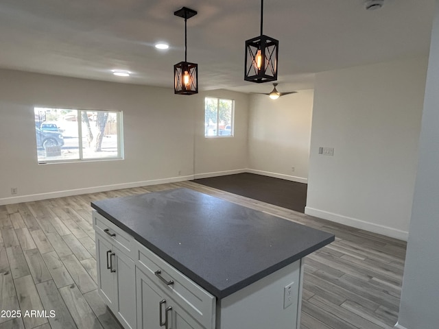 kitchen with ceiling fan, a kitchen island, light hardwood / wood-style flooring, pendant lighting, and white cabinets