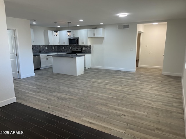 kitchen featuring light wood-type flooring, stainless steel appliances, decorative light fixtures, white cabinets, and a center island