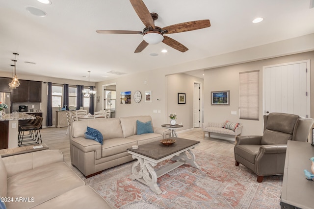 living room with ceiling fan with notable chandelier and light hardwood / wood-style flooring