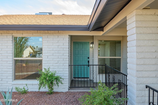 view of exterior entry with brick siding and roof with shingles